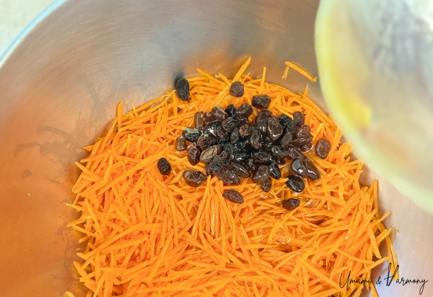 Julienned carrots and raisins in a bowl with dressing being poured