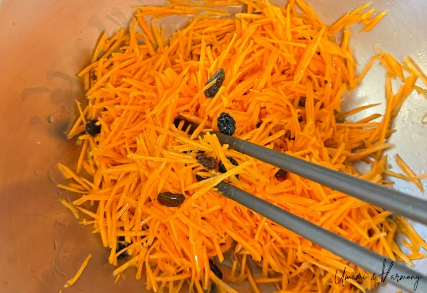 Tossing carrot salad with cooking chopsticks in a mixing bowl