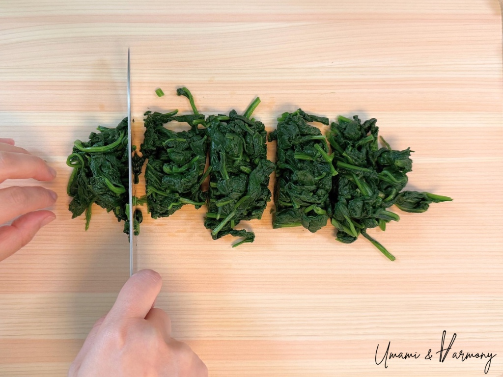 Spinach being cut into bite-sized pieces on a cutting board