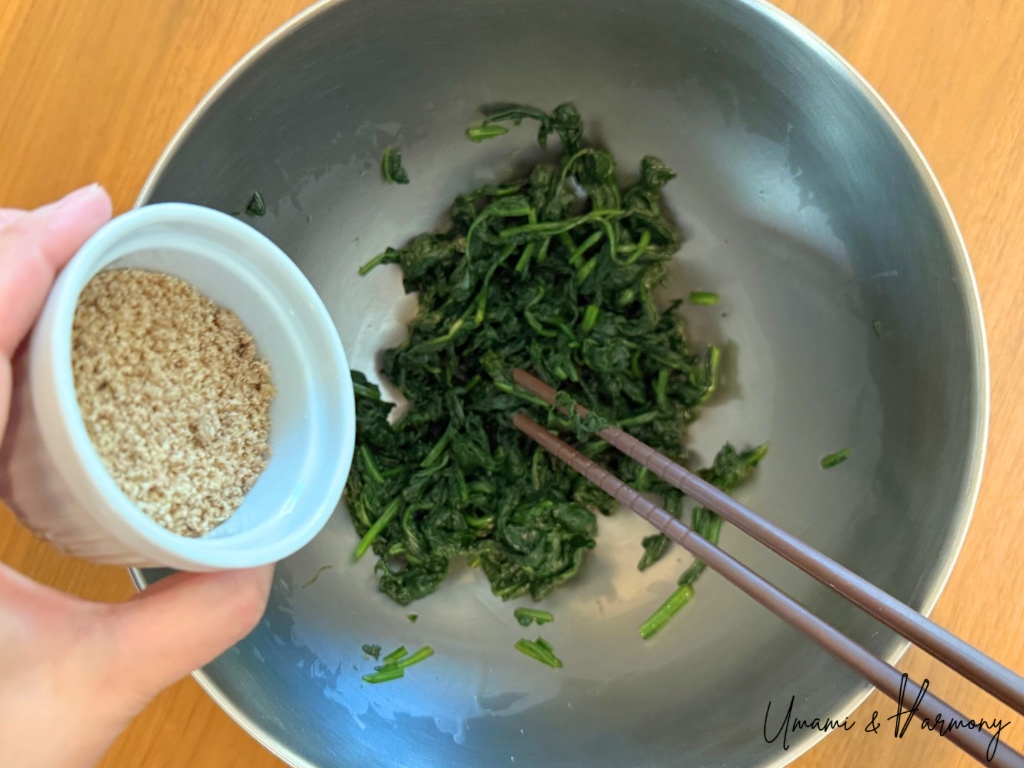 Ground sesame seeds being sprinkled over dressed spinach