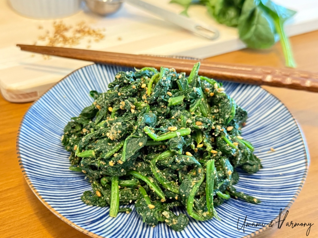 Japanese sesame spinach (goma-ae) served in a small dish with spinach and ingredients in the background