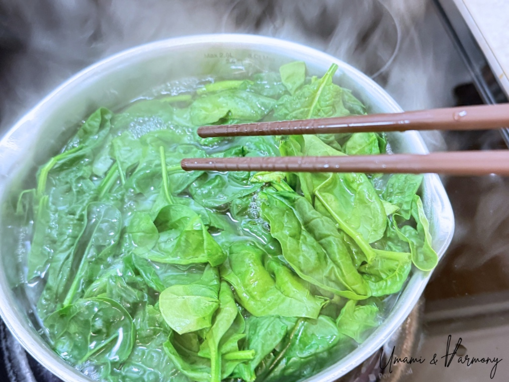 Spinach being blanched in boiling water with chopsticks stirring the pot