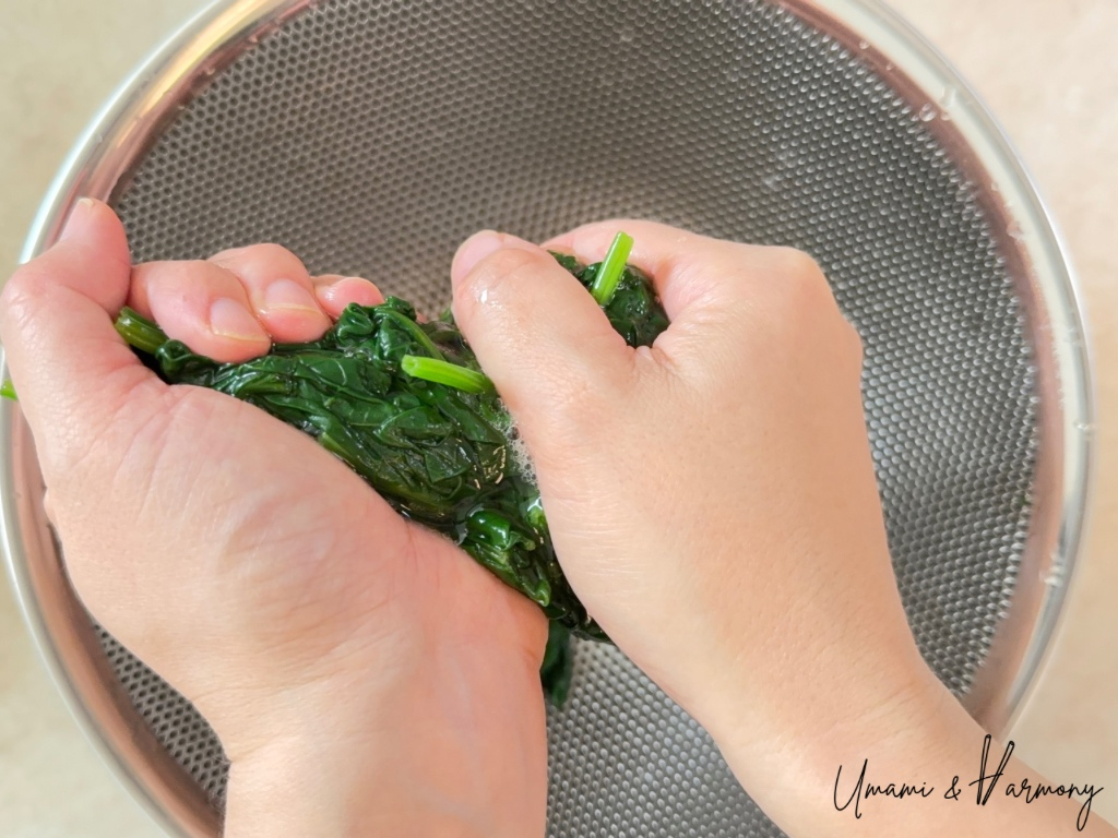 Hands squeezing excess water from spinach