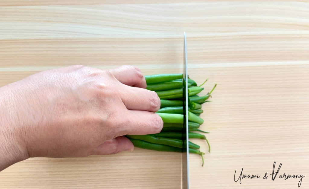 Raw green beans lined up with their stem ends being trimmed.