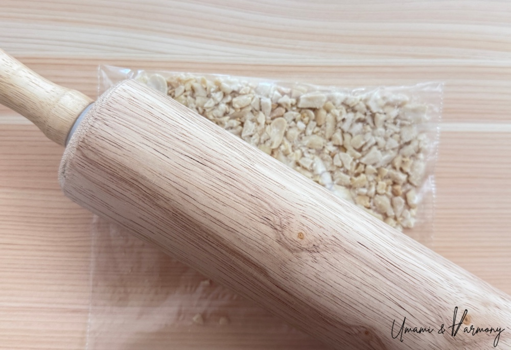 Whole peanuts in a plastic zip bag being crushed with a rolling pin.