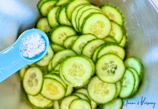 Salt being sprinkled over a bowl of sliced cucumbers