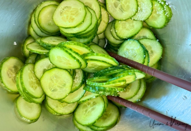 Chopsticks gently tossing salted cucumber slices in a bowl