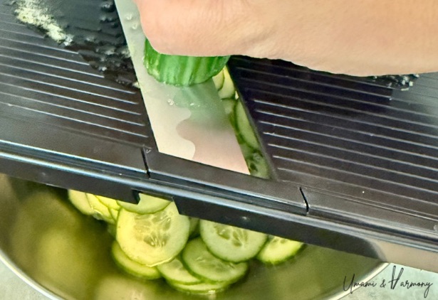 Hand slicing a cucumber into thin rounds using a mandoline slicer