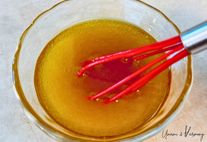 Small bowl with olive oil, vinegar, maple syrup, and salt being whisked to make salad dressing