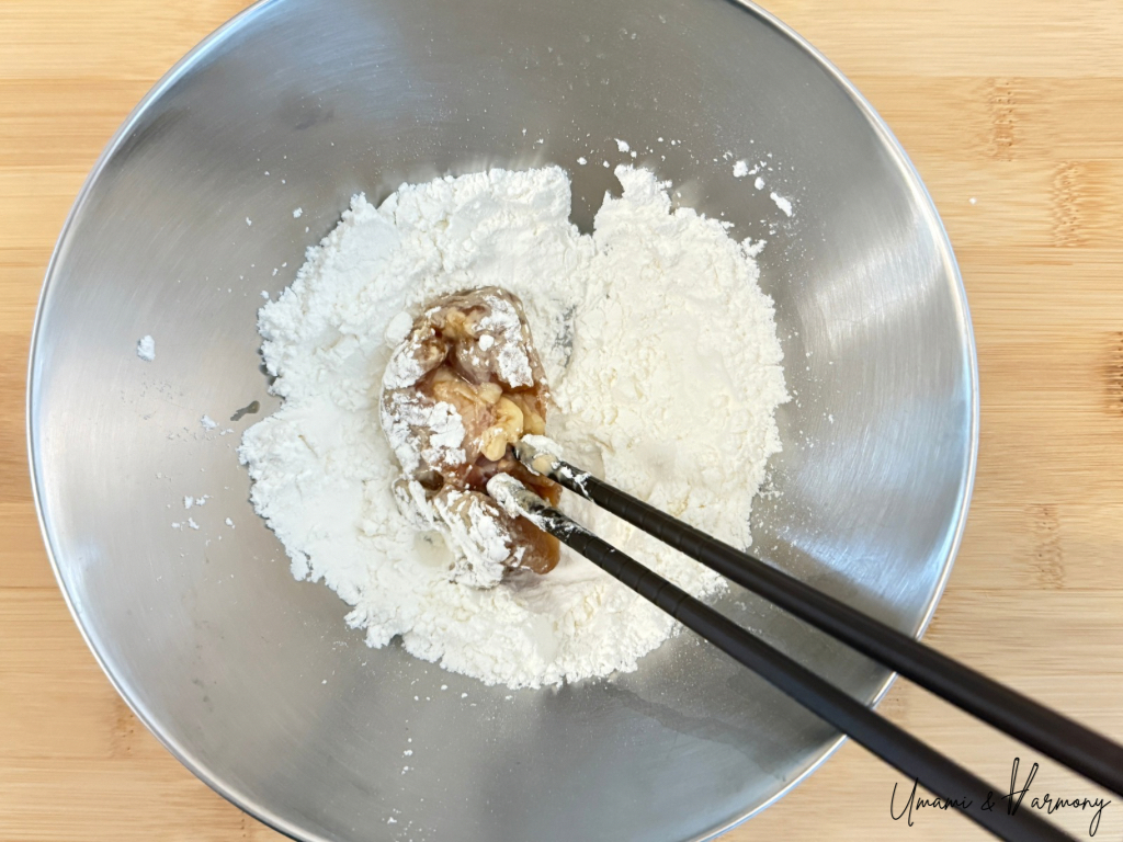 Marinated chicken pieces being coated in a flour and cornstarch mixture