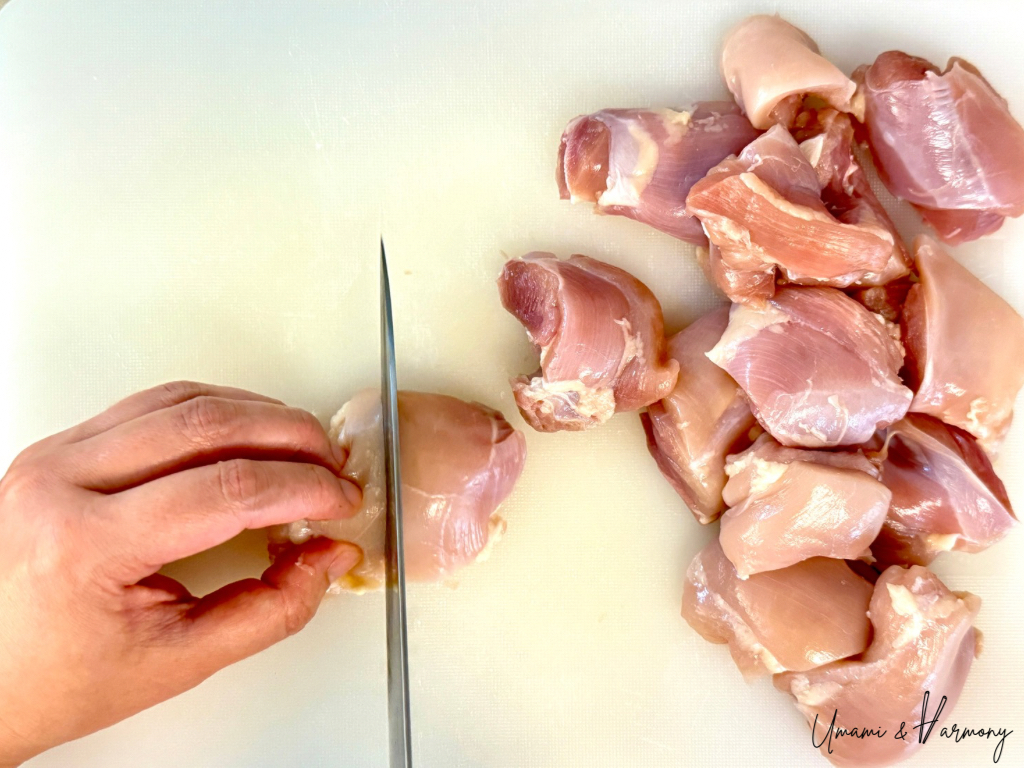Chicken thighs being cut into bite-sized pieces on a cutting board