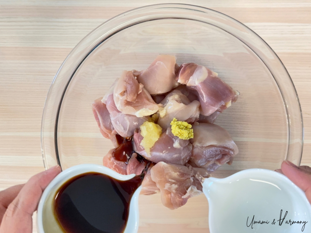 Ground garlic and ginger in a bowl with soy sauce and sake being poured over chicken