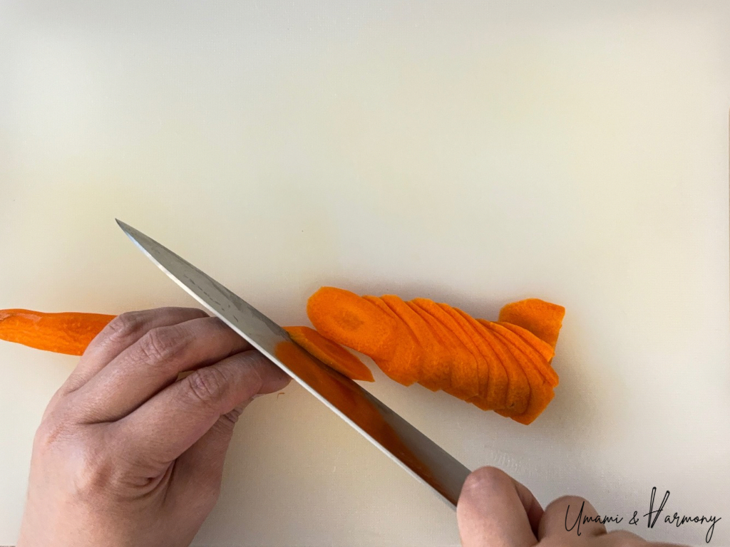 Carrot being thinly sliced diagonally on a cutting board