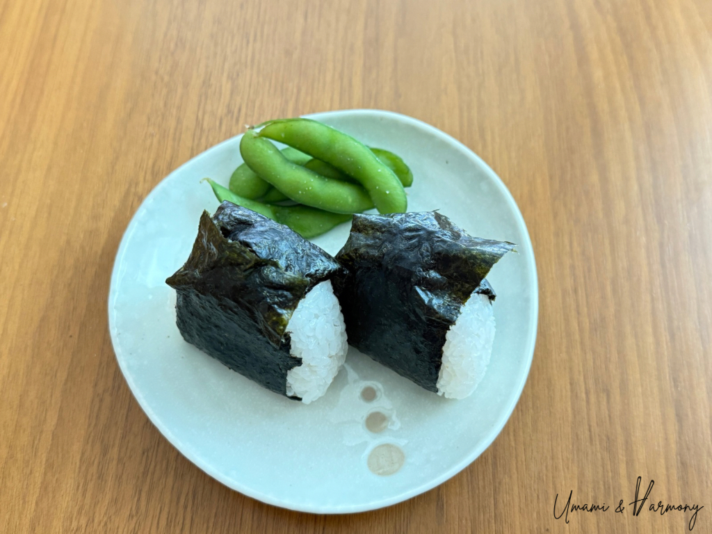 Two tuna mayo onigiri served on a small plate with edamame.