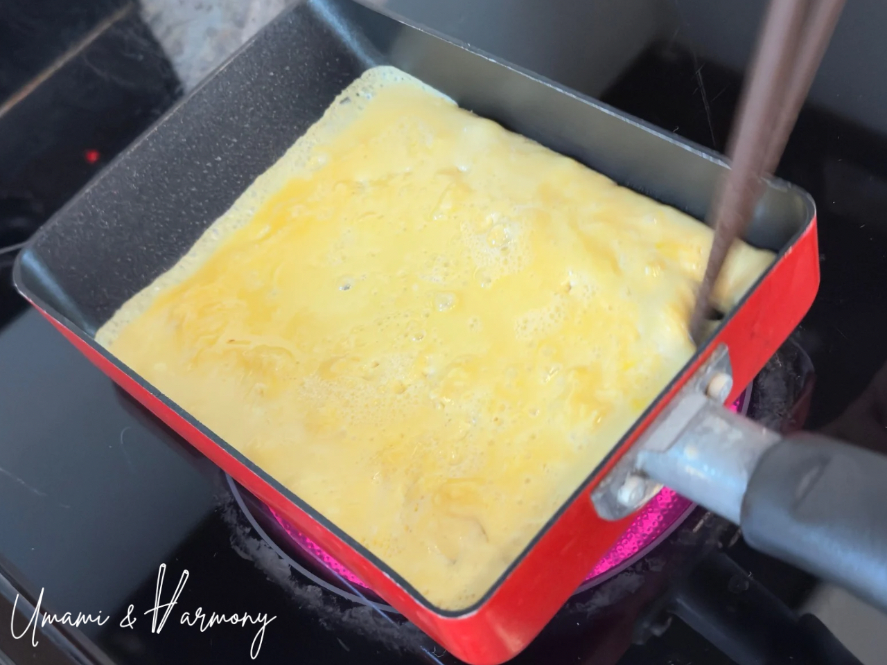 Tamagoyaki layer almost cooked, about to be rolled with chopsticks