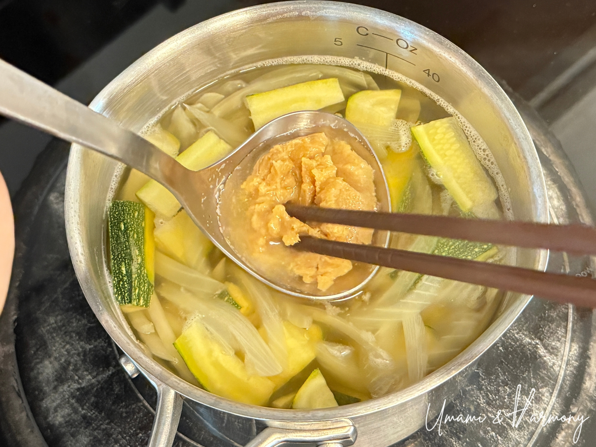 Miso paste in a ladle being dissolved into dashi stock with chopsticks