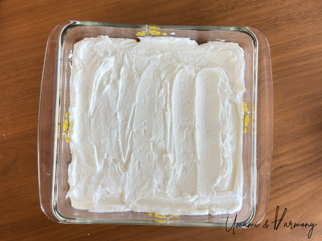Spreading half of the mascarpone cream mixture over the first layer of ladyfingers