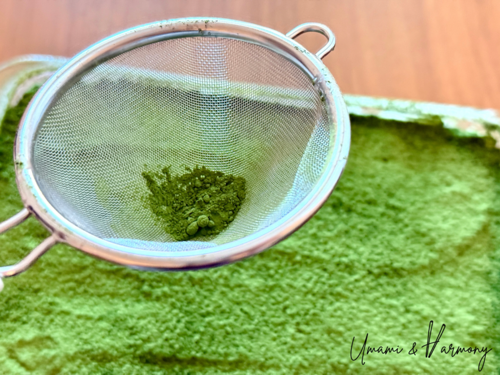 Dusting the top of Matcha Tiramisu with matcha powder using a fine tea strainer