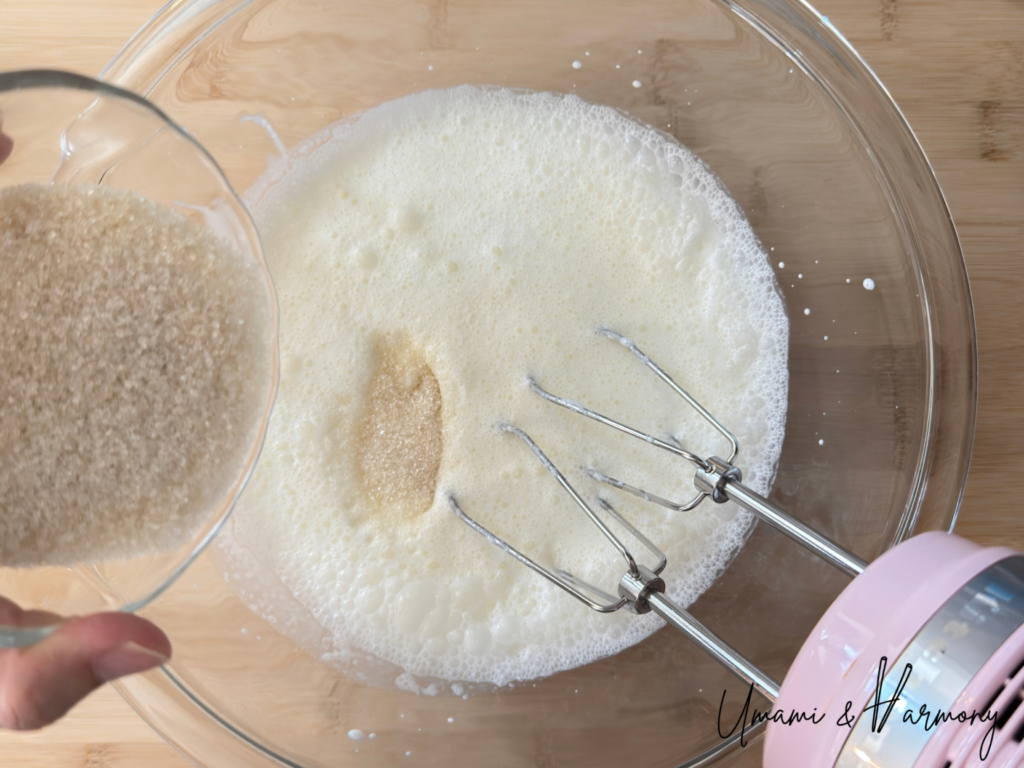 Whipping heavy cream in a bowl while adding sugar