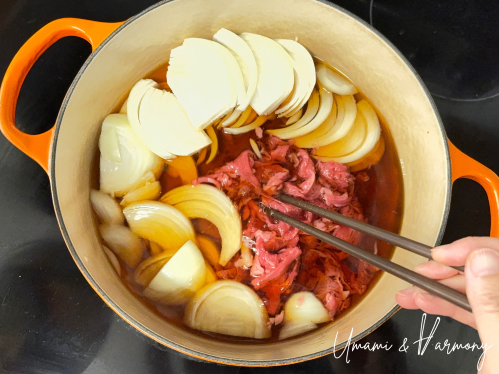 Adding shaved beef and onion to the dutch oven while loosening the beef