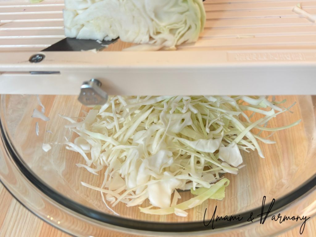 Cabbage being shredded with a slicer for sesame coleslaw