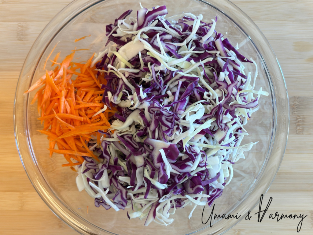 Shredded cabbage, red cabbage, and carrot in a glass mixing bowl