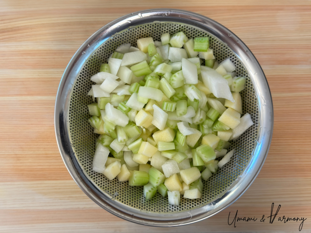Chopped onion, celery, and apple being drained in a colander