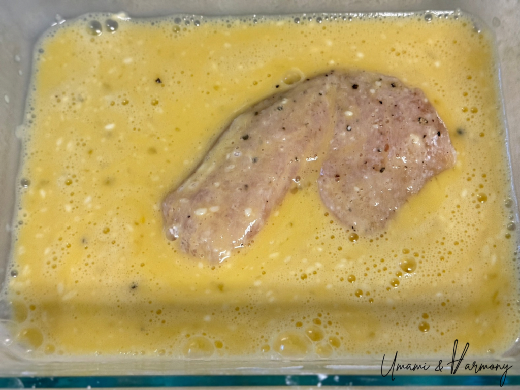 Chicken piece being dipped in the egg mixture