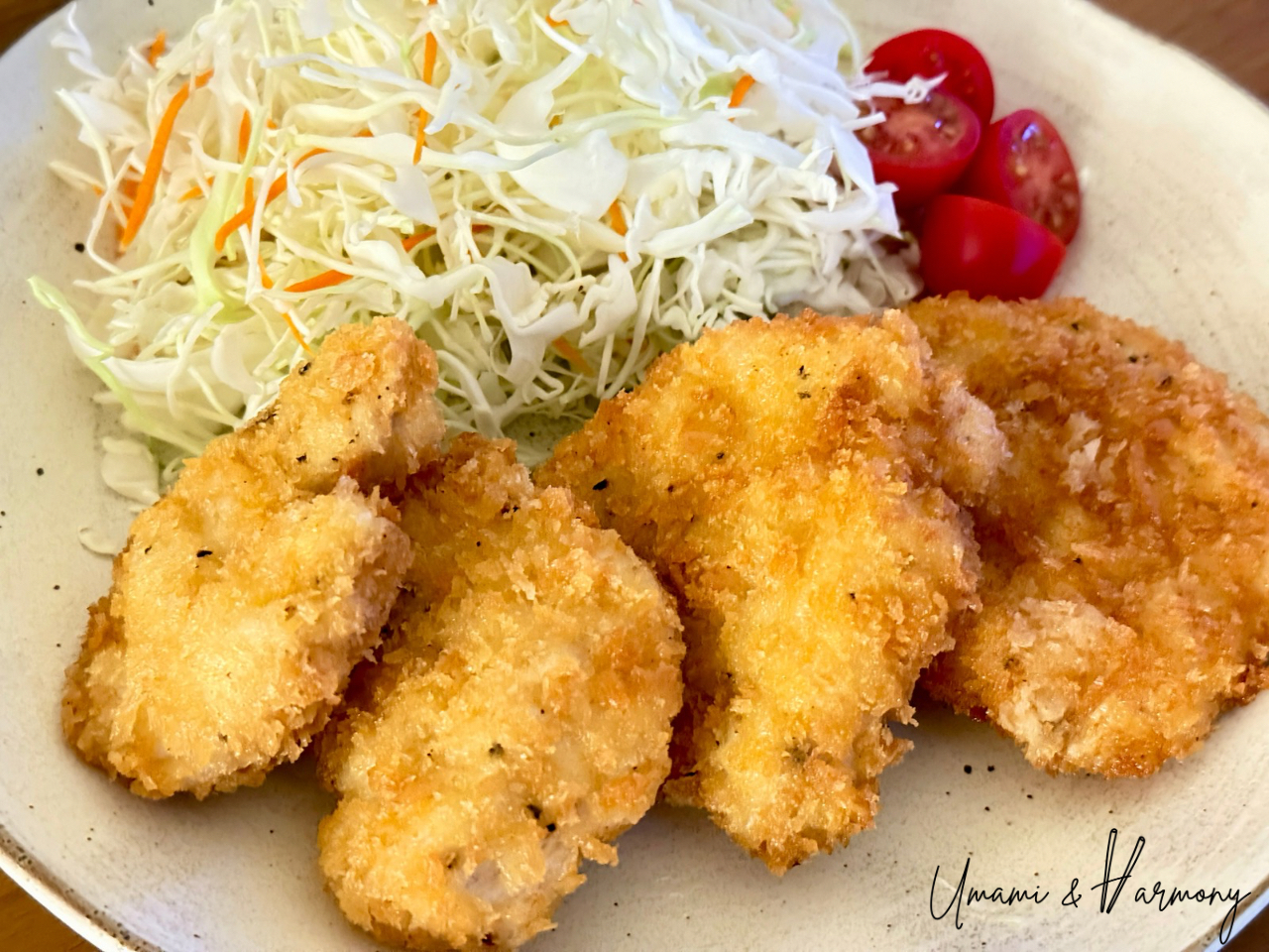 Chicken Katsu served on a plate with finely shredded cabbage and cherry tomatoes