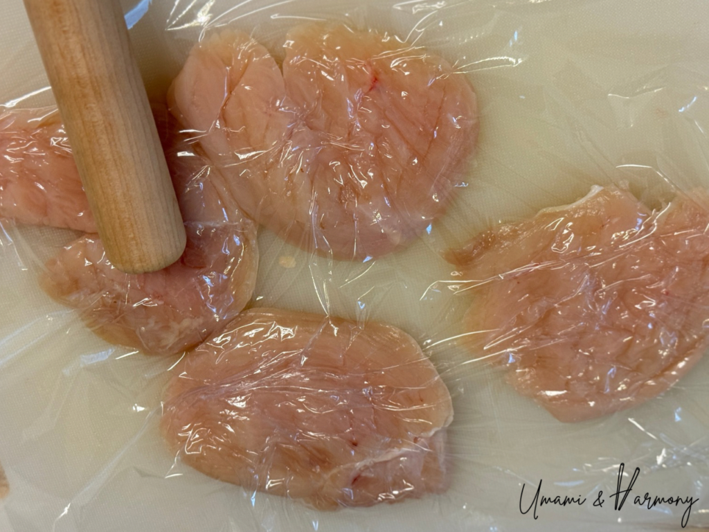 Chicken breast being pounded with a rolling pin to even thickness