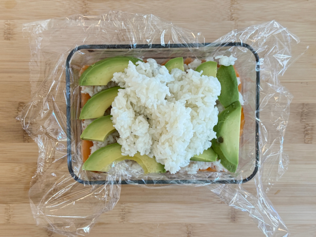 Sushi rice being spread evenly over avocado slices