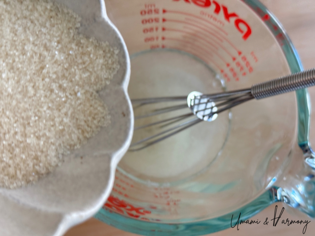 Sugar being added to a vinegar mixture in a small measuring cup