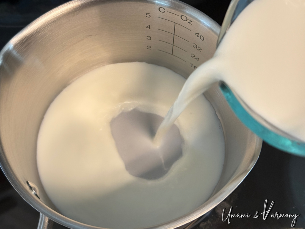 Milk and heavy cream being poured into a pot to make black sesame pudding