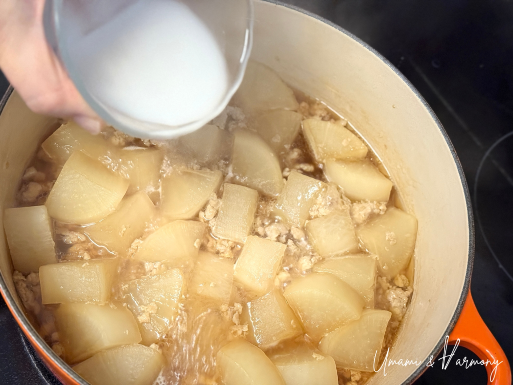 Cornstarch slurry being poured into simmered daikon to thicken sauce.