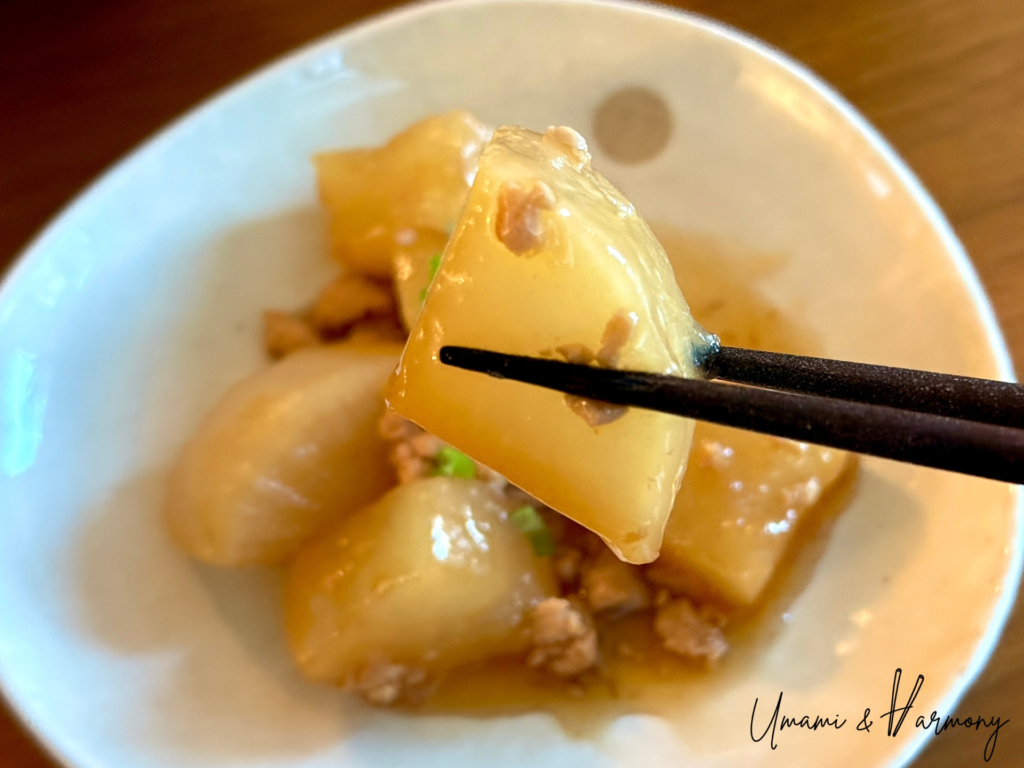 Japanese simmered daikon with chicken soboro being picked up with chopsticks