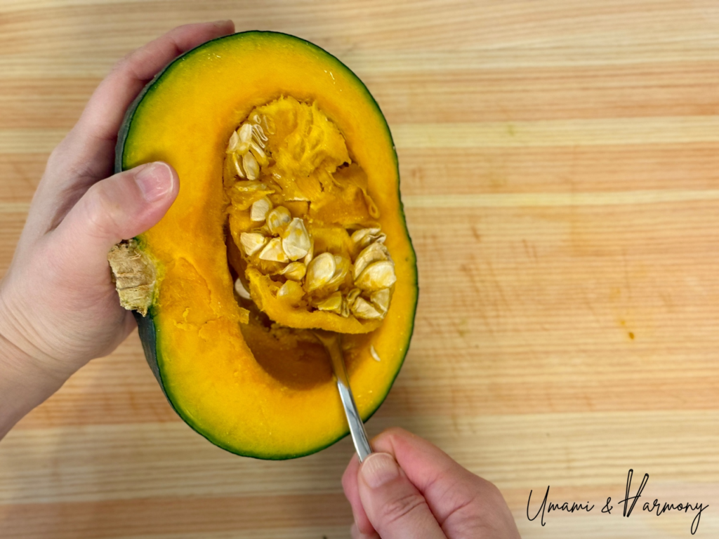 Whole kabocha squash cut in half and seeds are being removed with a spoon