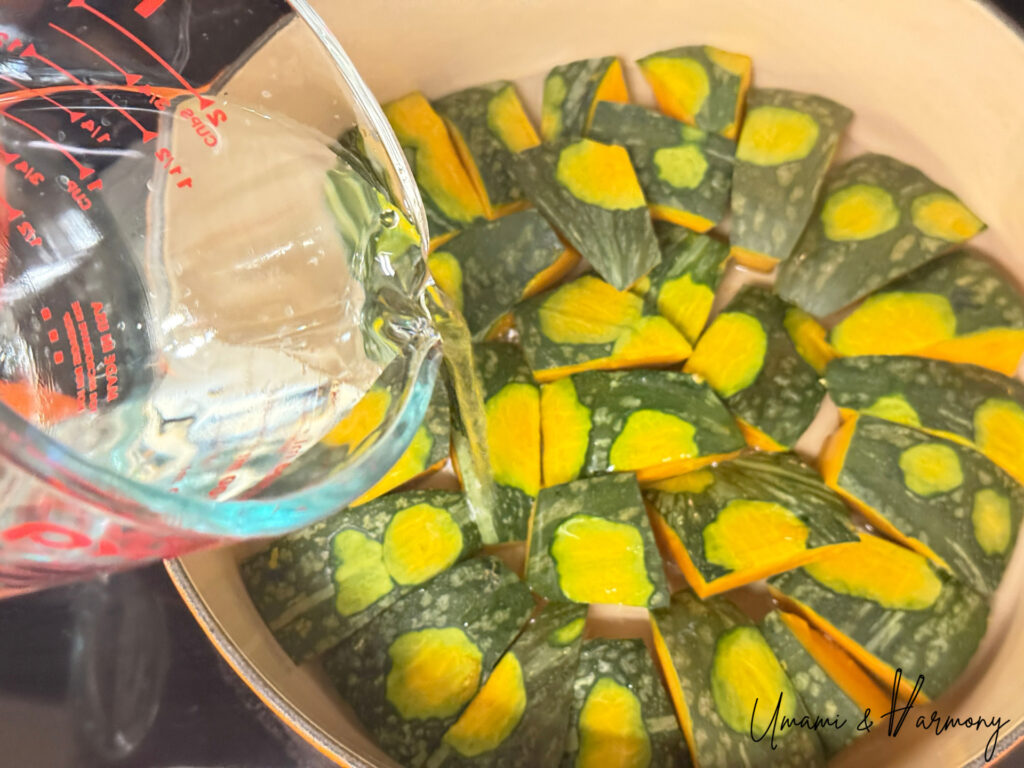 Water being poured into a pot filled with Kabocha pieces arranged skin-side up.