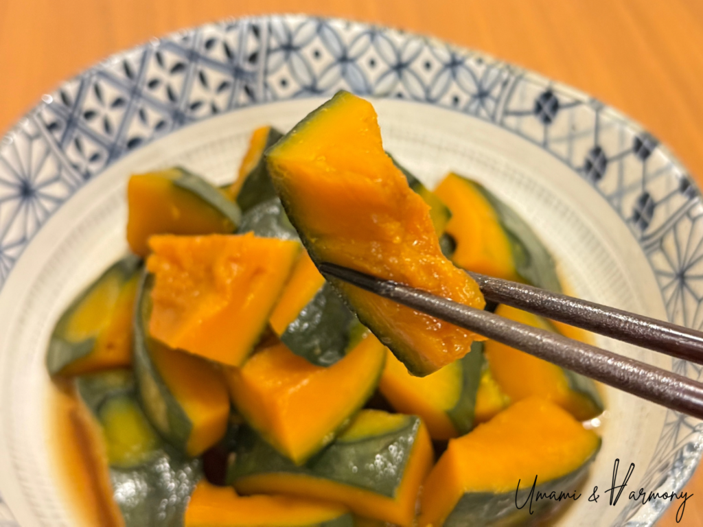 Braised Kabocha squash served on a plate with chopsticks holding a piece.