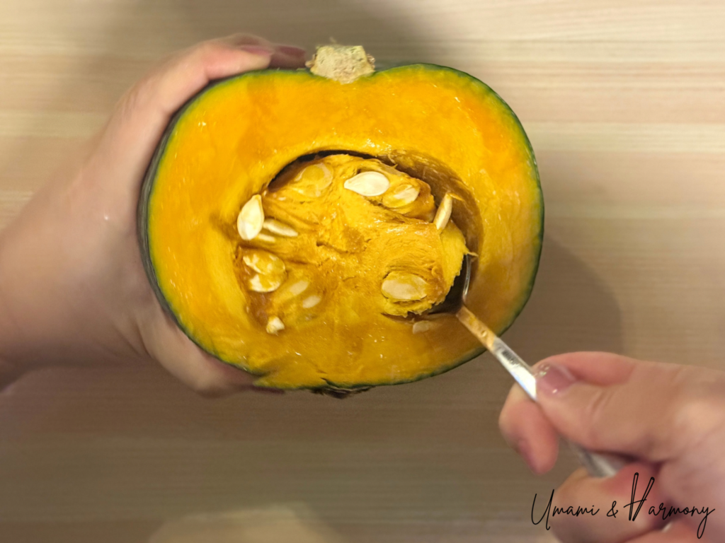 Seeds and fibers being scooped out of halved kabocha with a spoon