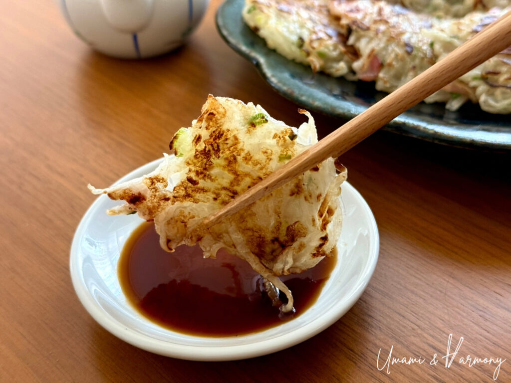 A piece of pan-fried daikon mochi picked up with chopsticks and about to be dipped in soy sauce