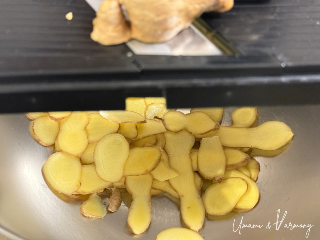 Ginger being thinly sliced with a kitchen slicer