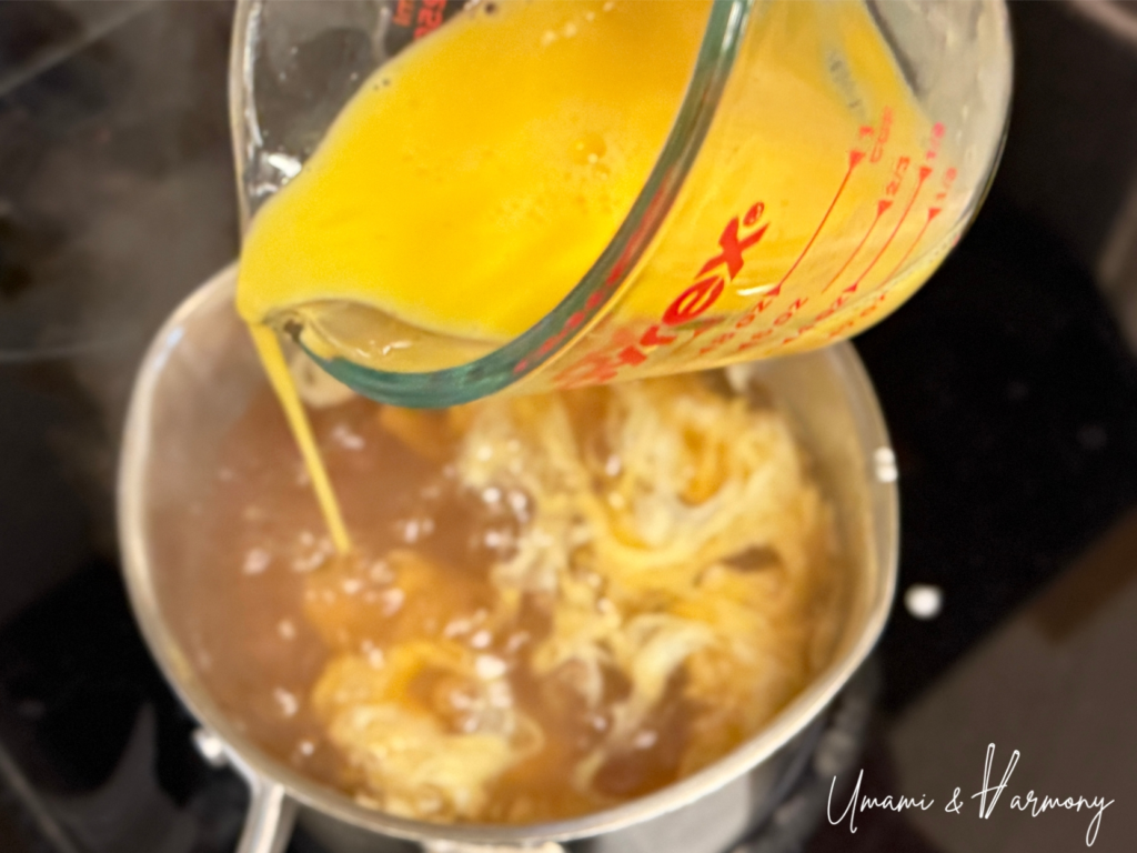 Beaten eggs poured slowly into hot dashi in a circular motion