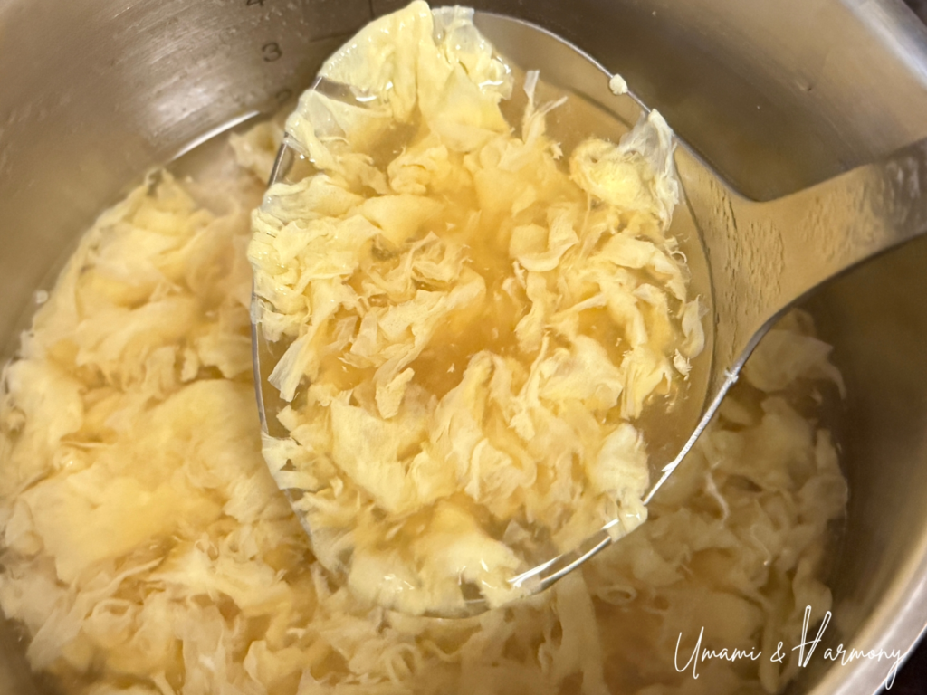 Ladle gently stirring soup from the bottom to create fluffy egg ribbons