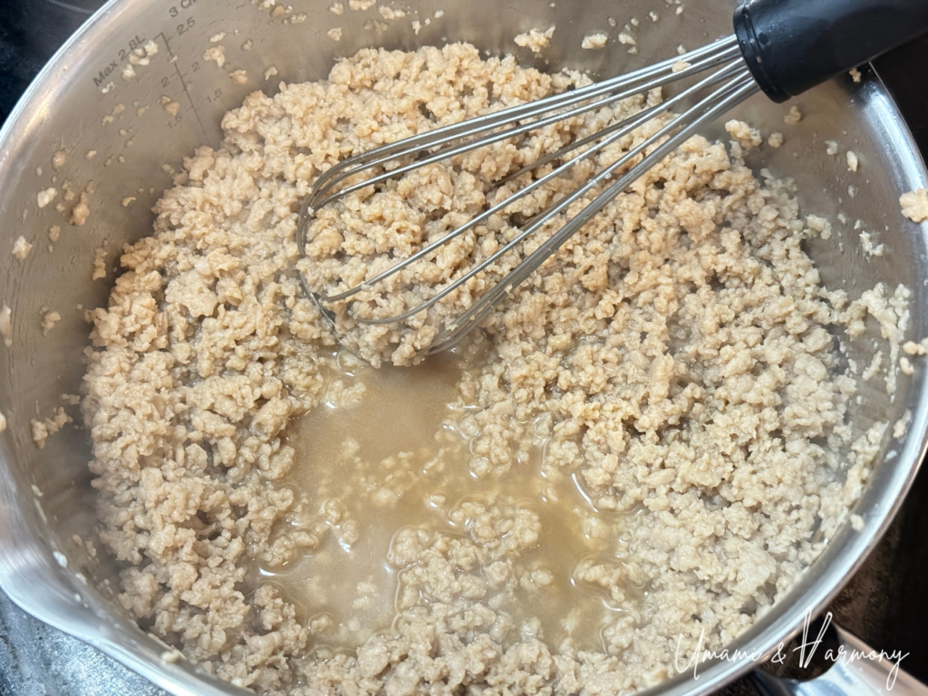 Ground chicken being cooked and stirred with a whisk as juice is released