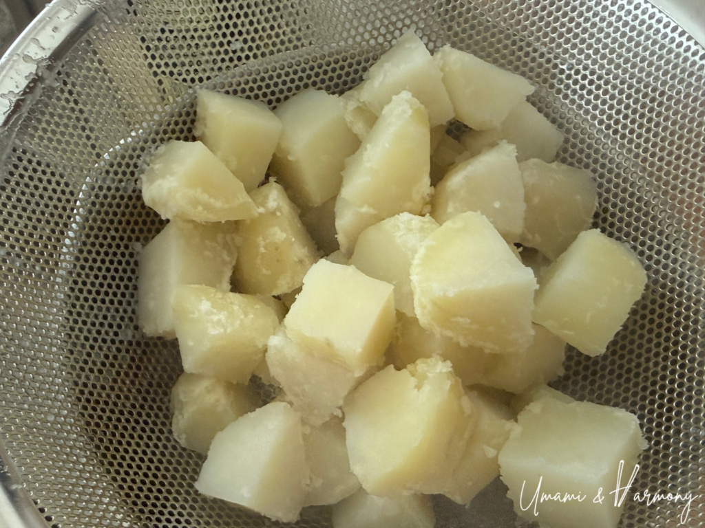 Boiled potato pieces being drained in a strainer
