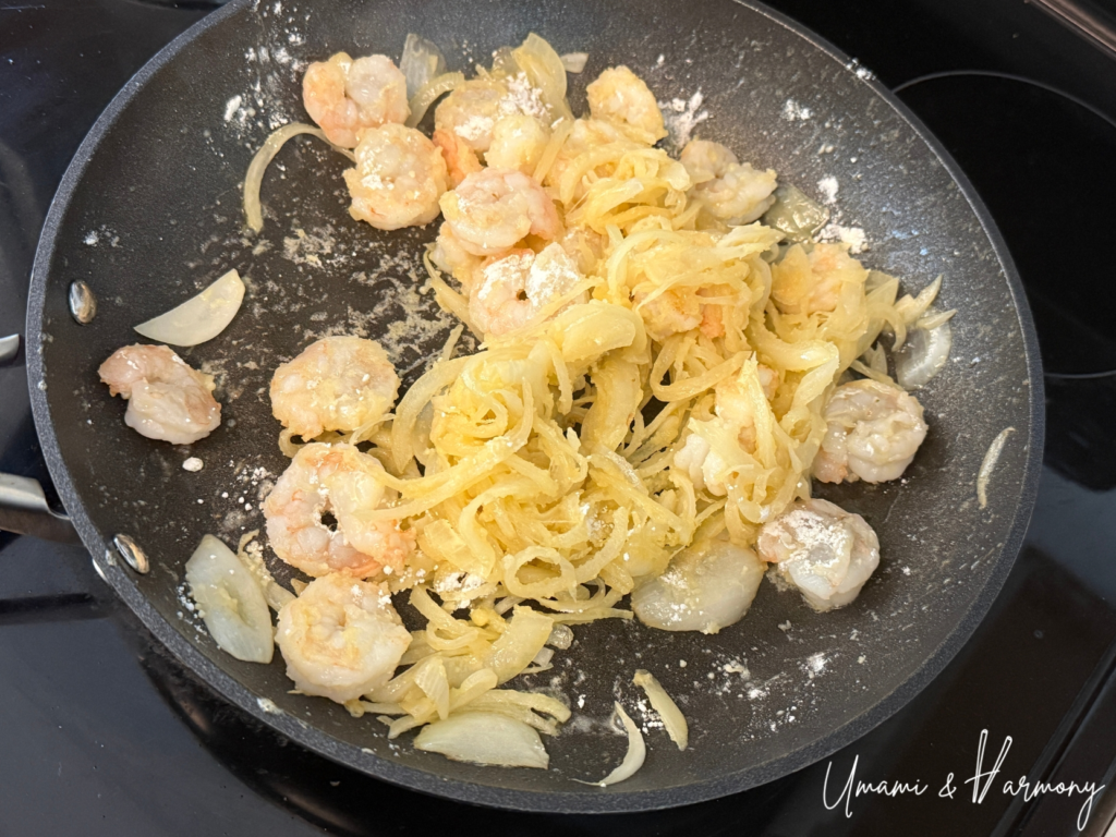 Shrimp and onion being sautéed in a pan after flour is fully incorporated