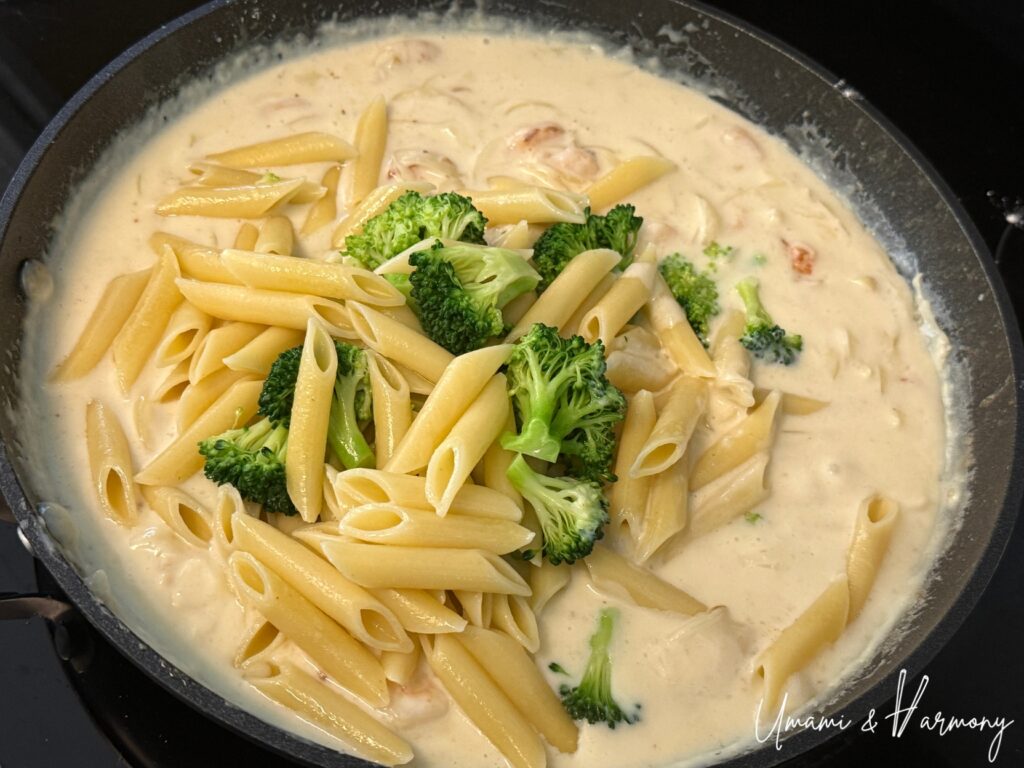 Penne pasta and broccoli being added into the creamy sauce