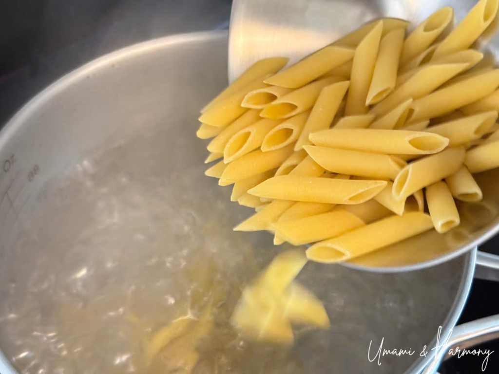 Penne pasta being added to a pot of boiling water
