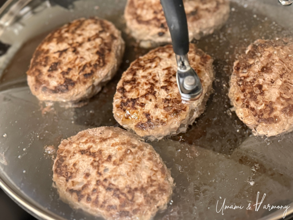 Hamburg steak cooking in a pan covered with a glass lid over low heat