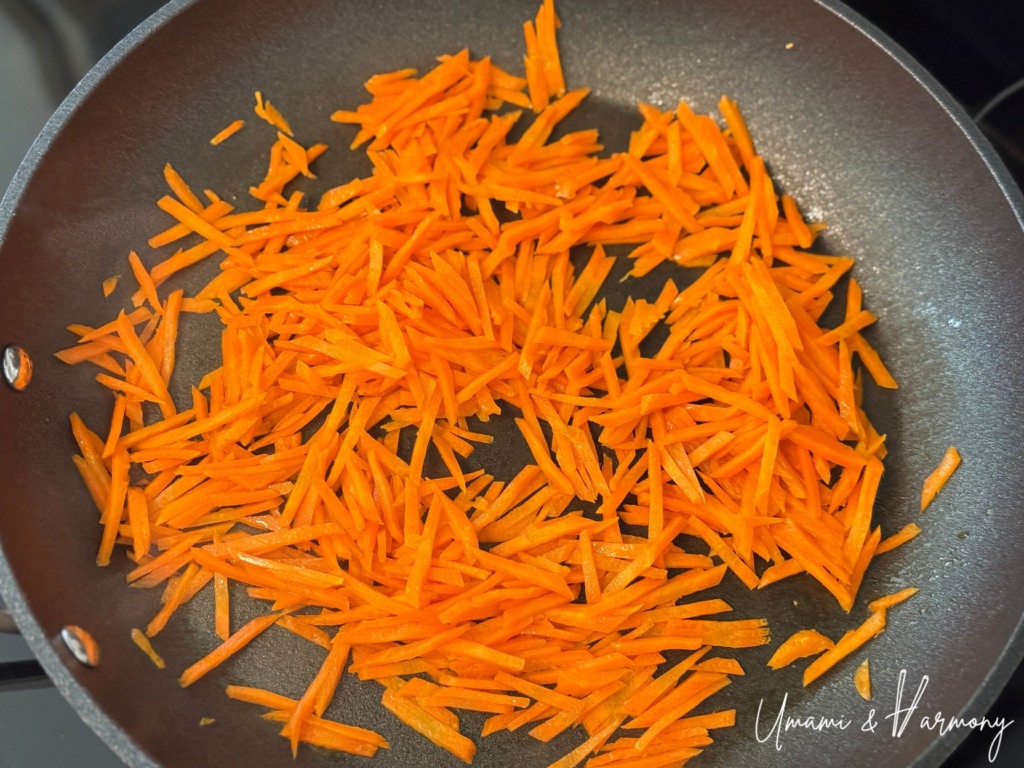 Julienned carrots being sautéed in a pan